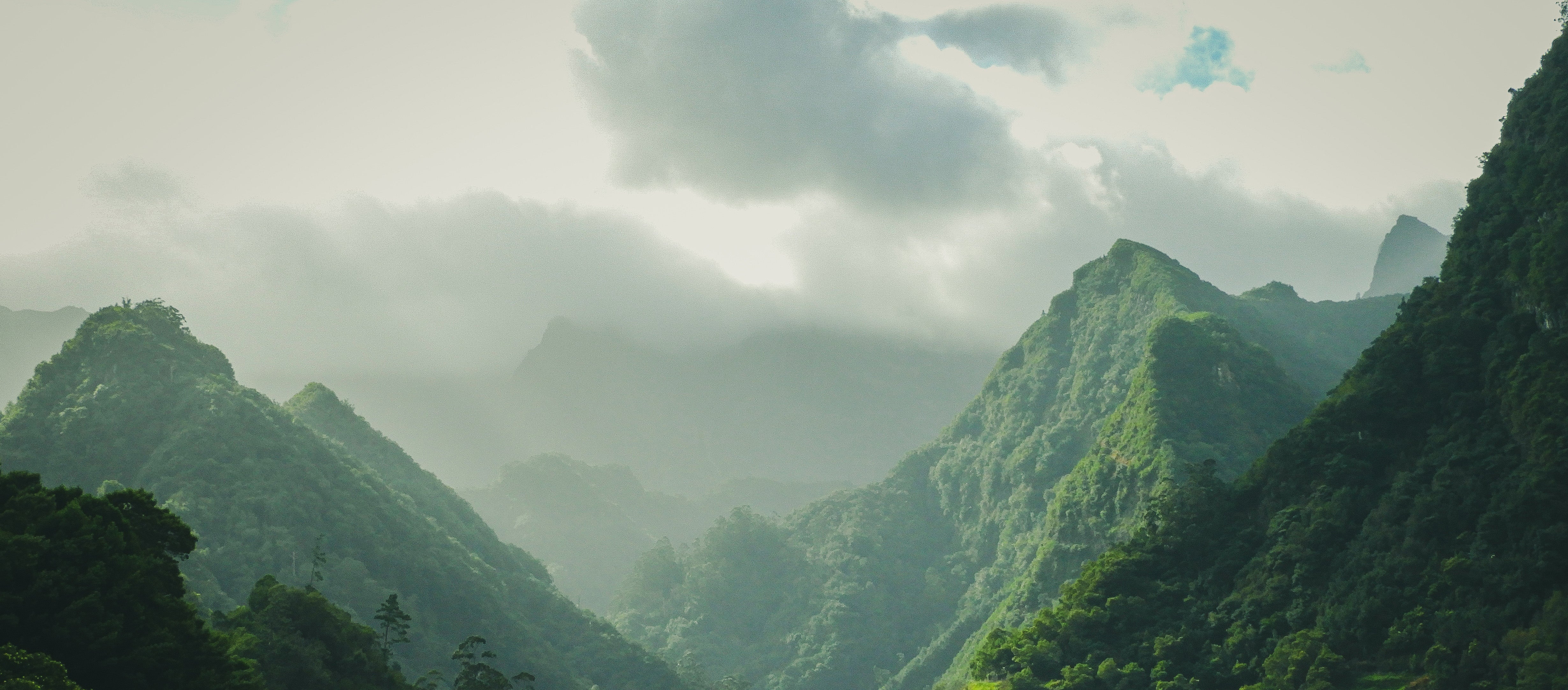 Lush green mountains partially covered in mist under a cloudy sky, evoking a serene and natural atmosphere — background for the text "Unsere Verantwortung" (Our Responsibility).