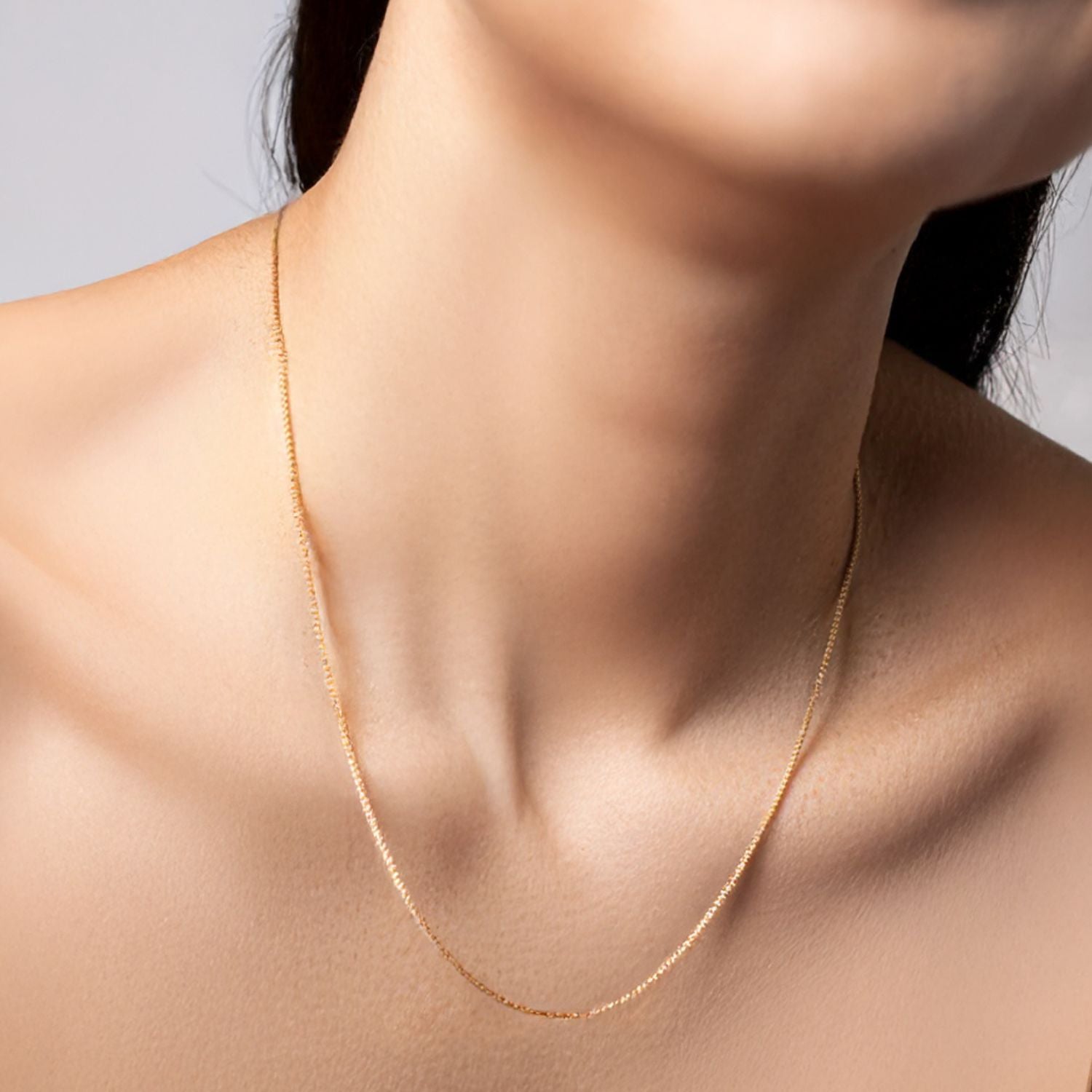 Close-up of a woman wearing a fine gold box chain necklace, displayed elegantly on her neck, minimal and refined jewelry look.