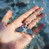 Nessie Fin pendant by Seinerzeit – ocean-inspired sterling silver jewelry with blue and white CZ stones, shaped like a whale tail and photographed in hand in the sea
