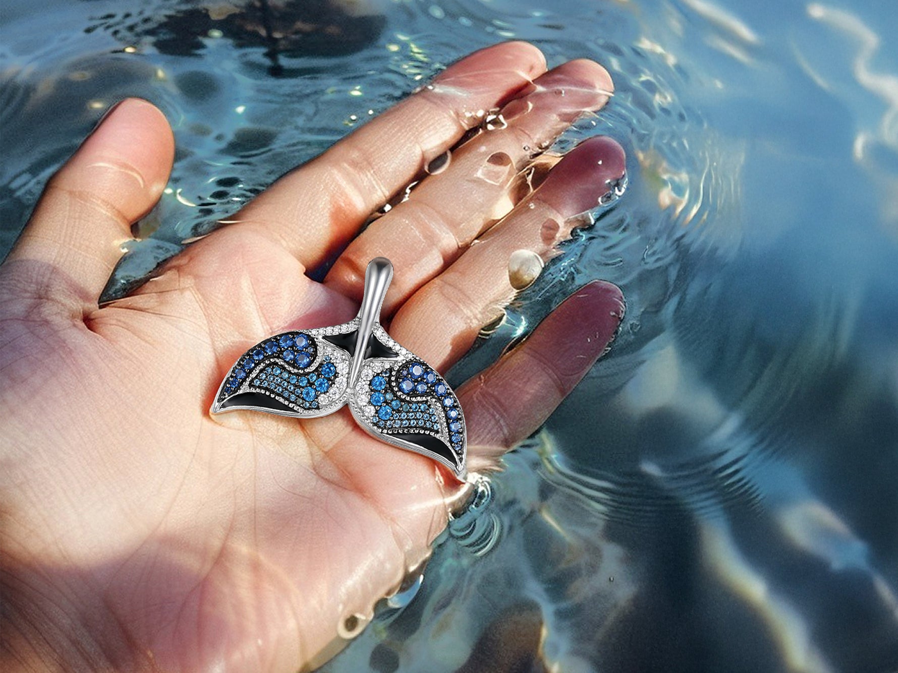 Nessie Fin pendant by Seinerzeit – ocean-inspired sterling silver jewelry with blue and white CZ stones, shaped like a whale tail and photographed in hand in the sea
