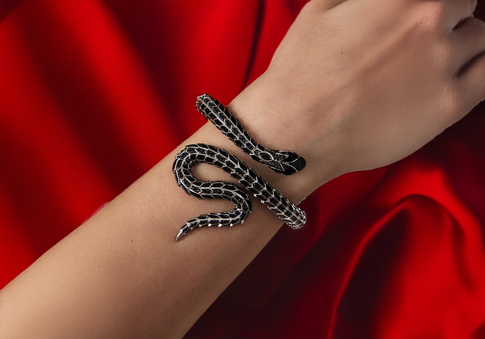 Stimmungsbild. Ein Arm wird mit dem schwarzen Eragon Schlangenarmreif dargestellt. Die Perspektive ist von oben und zeigt die volle Pracht der Armspange. Hintergrund ist ein rotes Tuch.