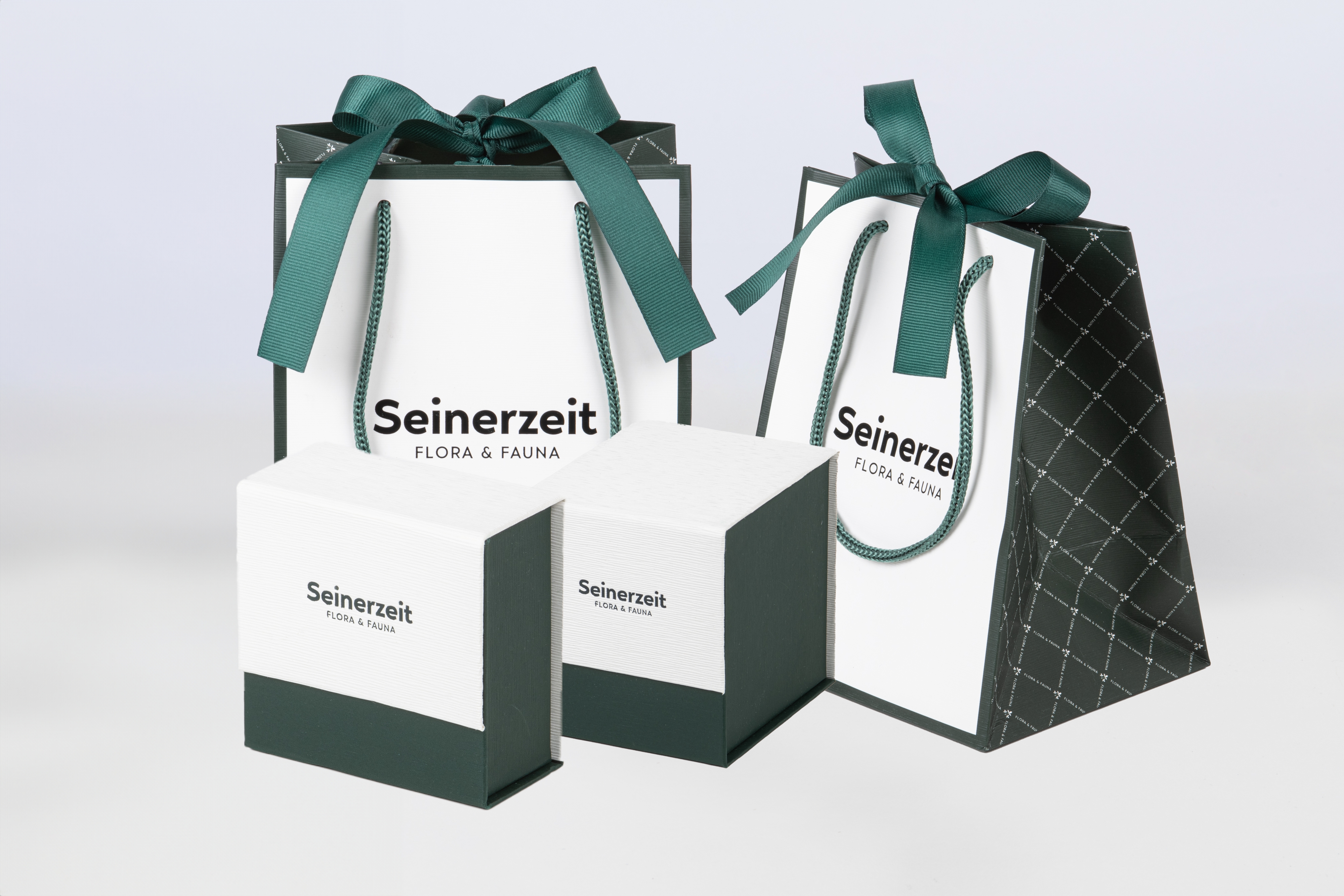 Seinerzeit Flora & Fauna luxury jewelry packaging, featuring two dark green and white gift bags with ribbon handles and two matching jewelry boxes.