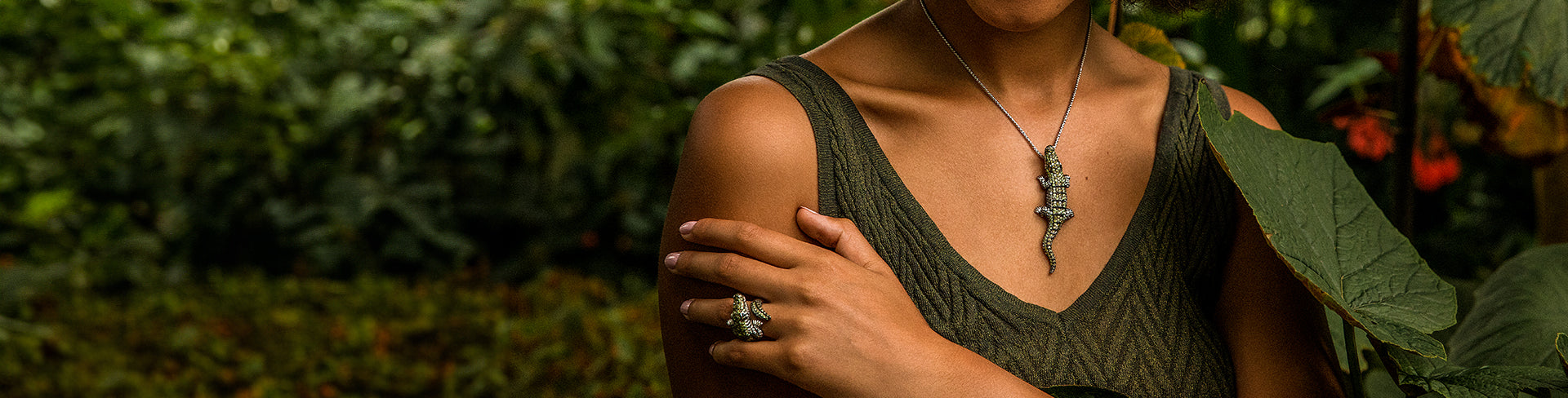 Woman wearing the Seinerzeit charles crocodile pendant in silver with green cubic zirconia accents, paired with a matching crocodile ring, styled against a lush jungle background.