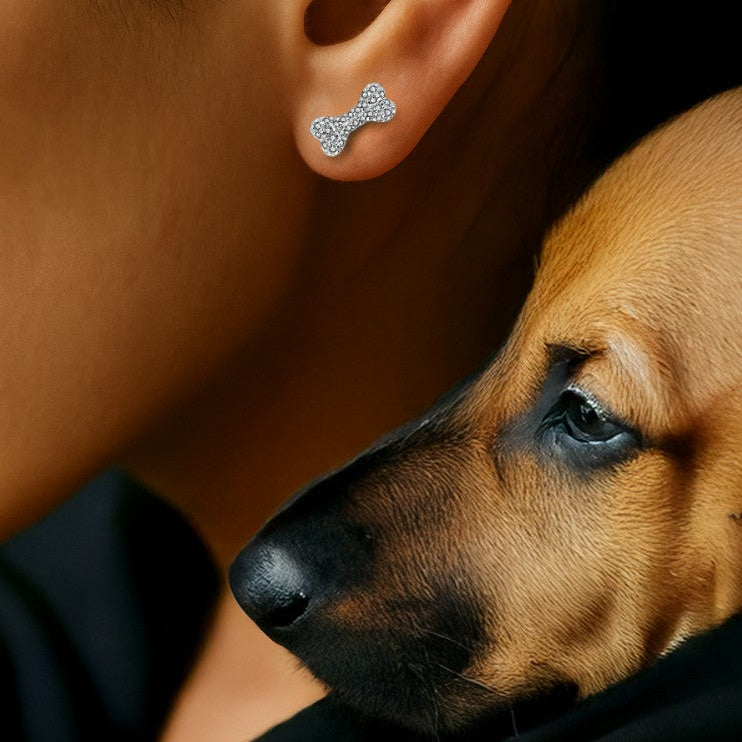 Close-up of a woman wearing bone-shaped stud earrings encrusted with clear cubic zirconia stones, while holding a brown puppy close to her face.