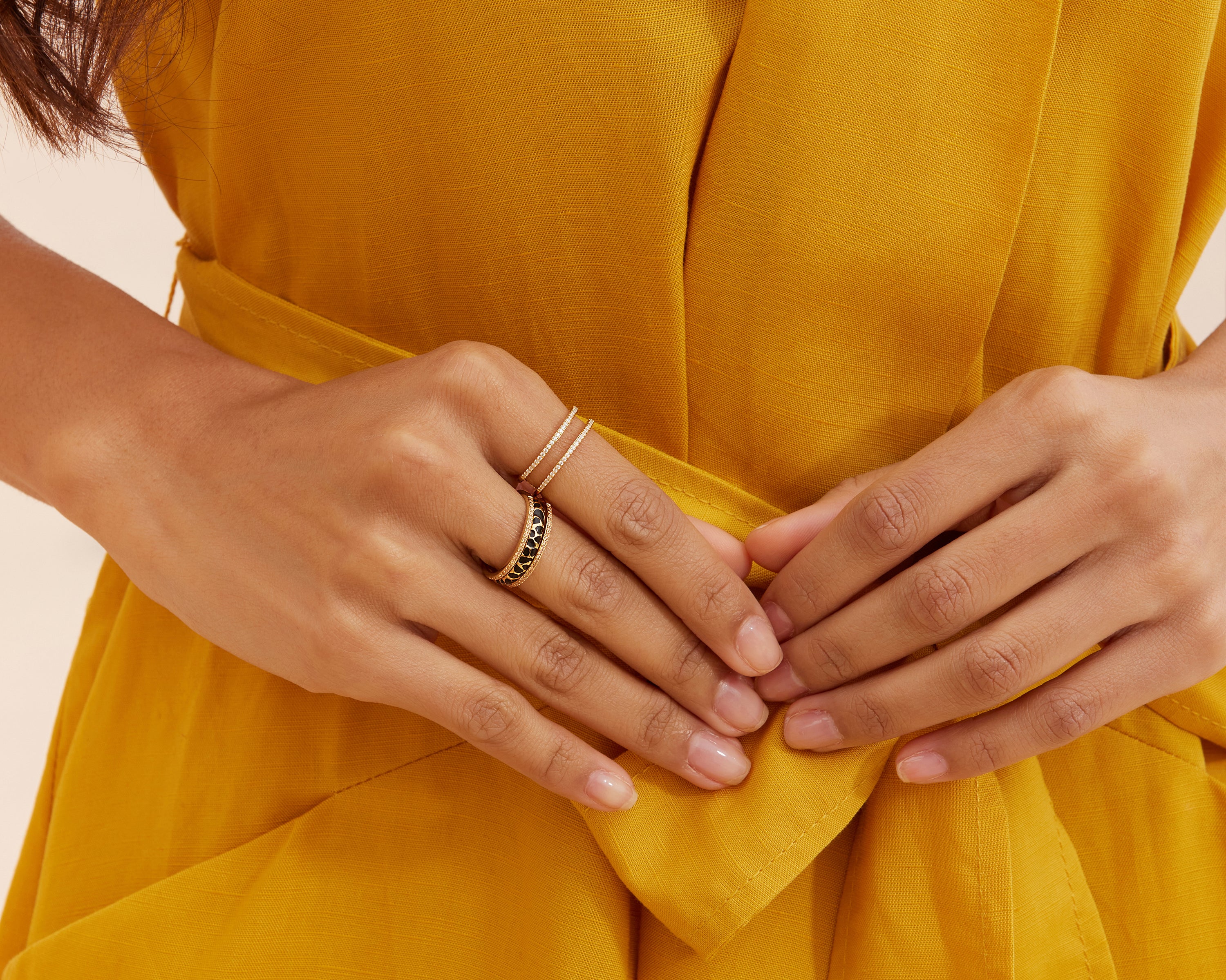 Close-up of hands wearing the Seinerzeit Flora & Fauna Sunshine Ring paired with the Kiani Leopard Ring in an enhancer combination style, styled with a mustard yellow wrap dress.