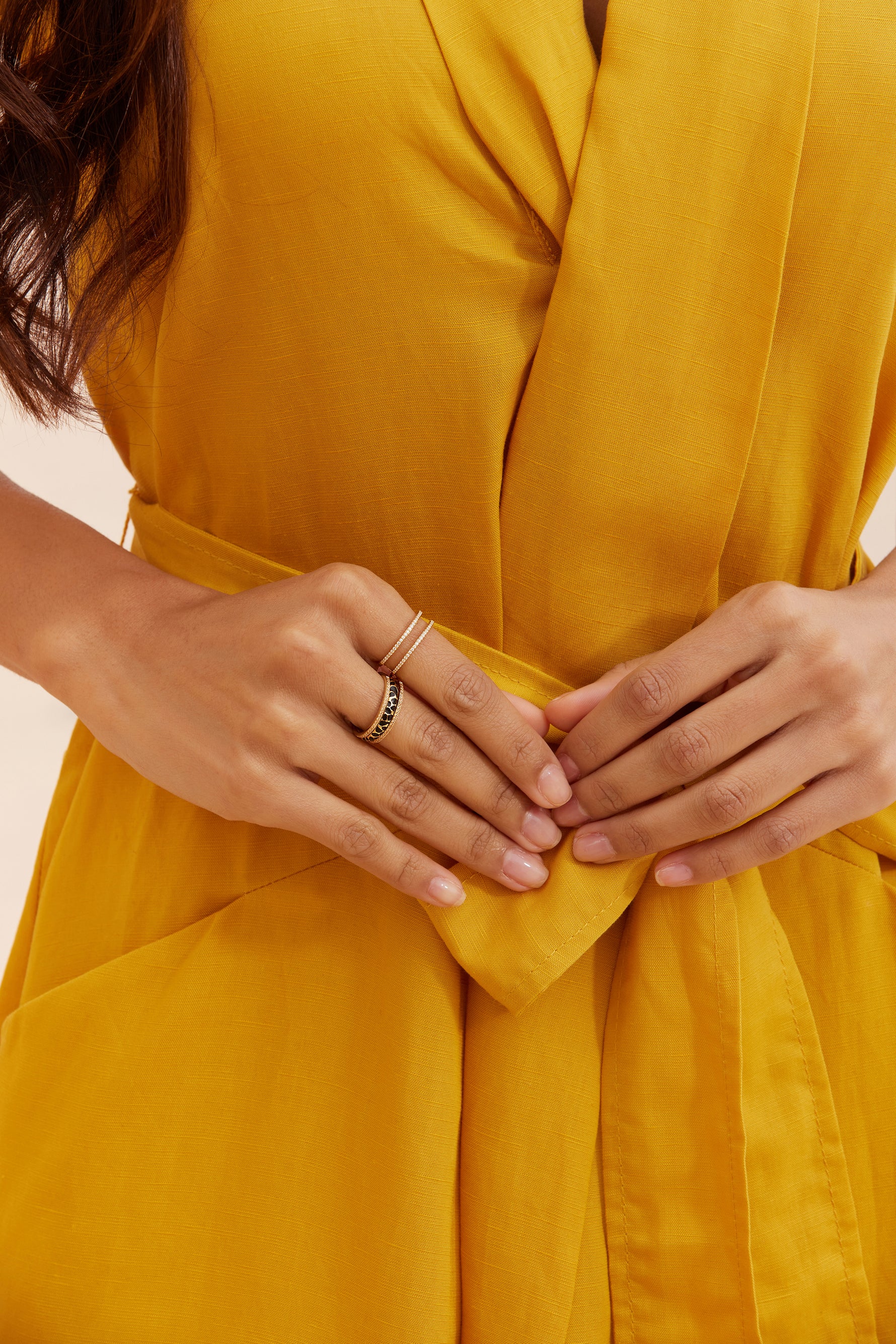 Close-up of hands wearing the Seinerzeit Flora & Fauna Sunshine Ring paired with the Kiani Leopard Ring in an enhancer combination style, styled with a mustard yellow wrap dress.